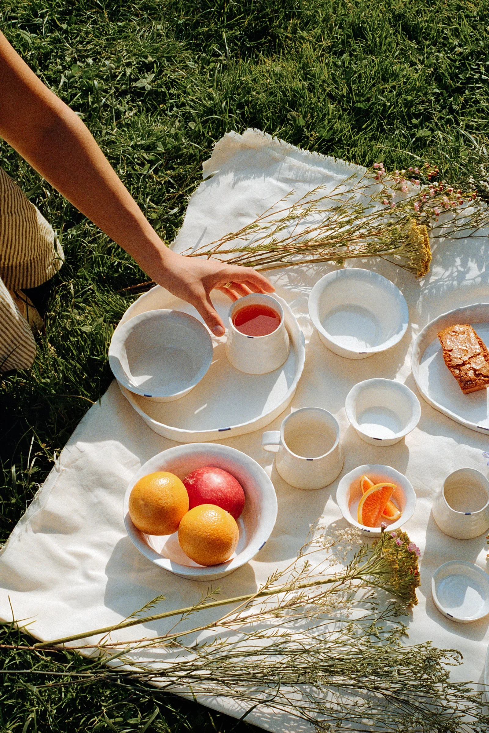 Picnic spread of white ceramics, fruit, pastries, and flowers