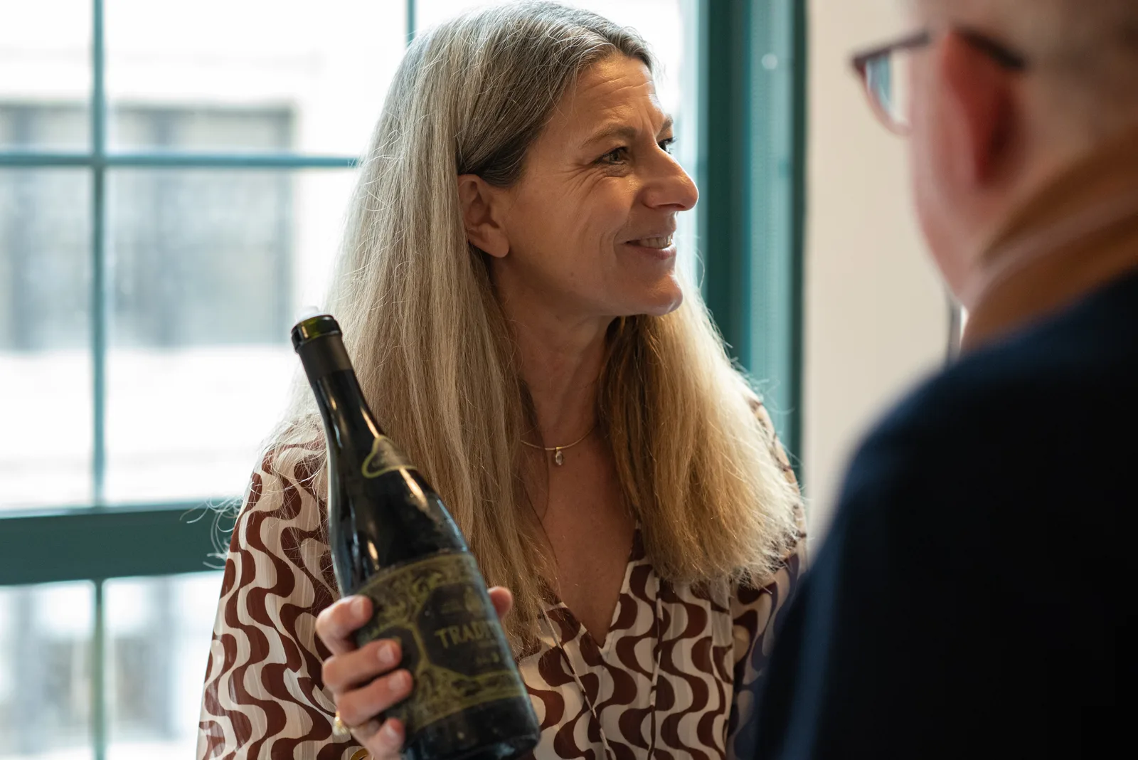 Woman holding a bottle while speaking to a guest at a wine tasting
