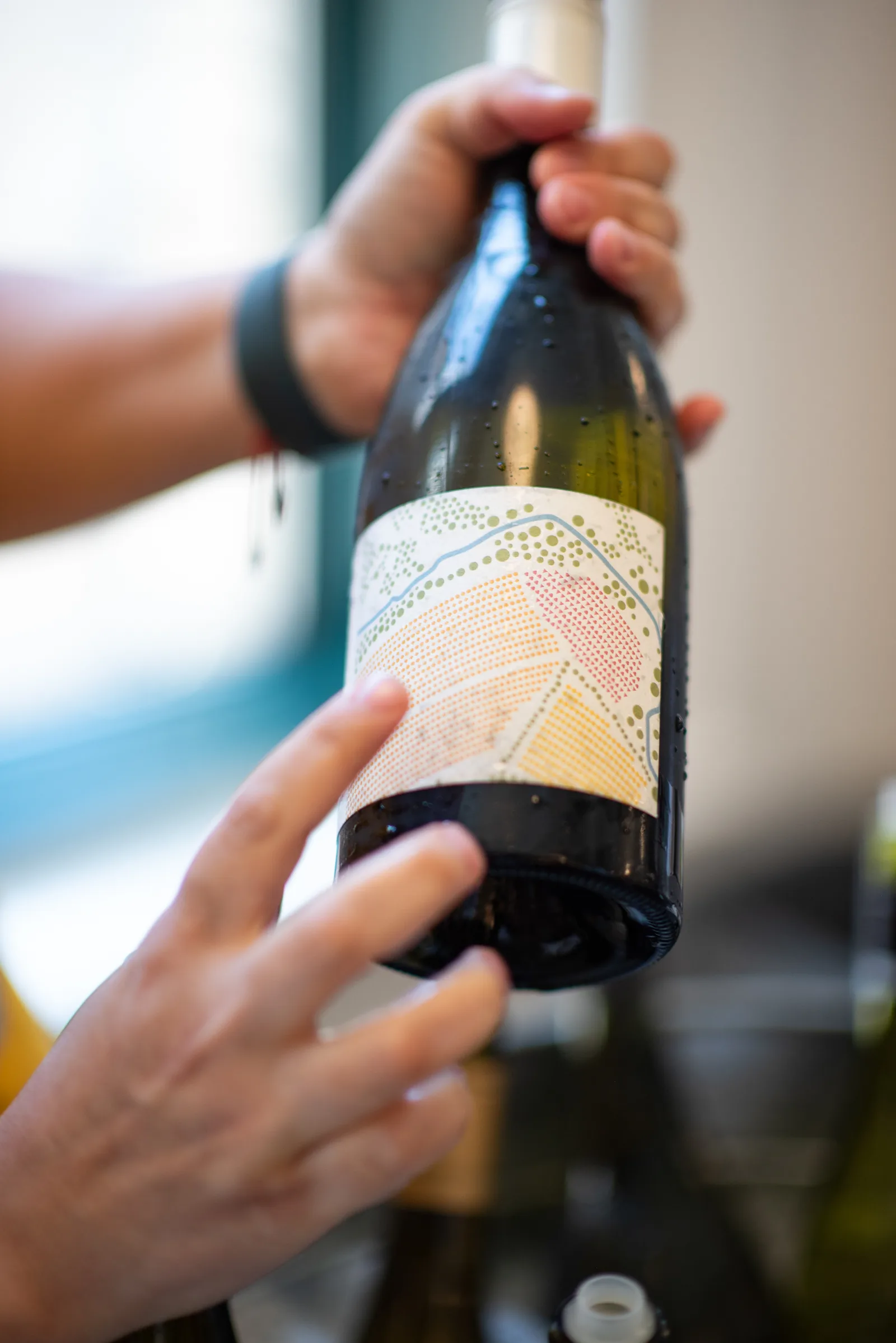 Hands presenting a wine bottle with a colorful patterned label